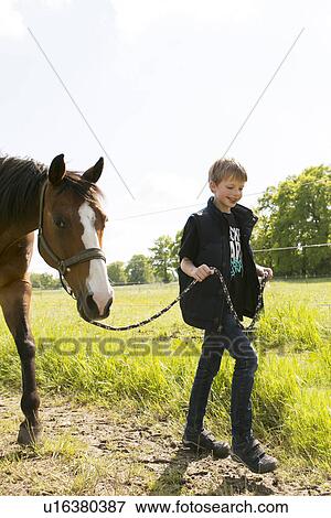 Smiling boy leading horse along dirt track View Large Photo Image Stock Photo - Smiling boy leading horse along dirt track. Fotosearch