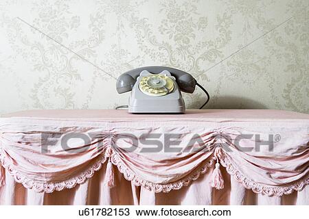 Stock Image - Still life of vintage telephone on frilly tablecloth. Fotosearch