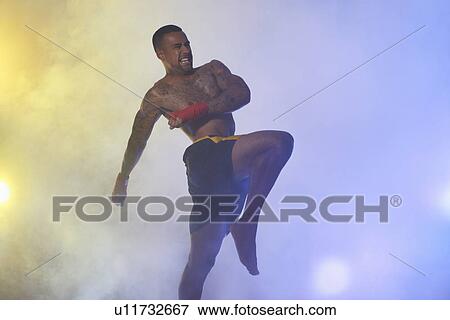 Stock Photo - Studio shot of muscular male kickboxer in spotlights and mist. Fotosearch
