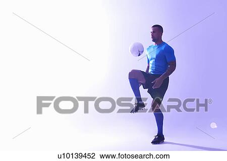 Stock Image - Studio shot of young male soccer player keeping ball mid air with knee. Fotosearch