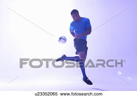 Stock Photography - Studio shot of young male soccer player keeping ball mid air with back kick. Fotosearch