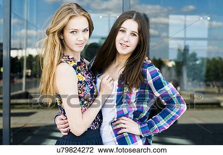Stock Image - Tender portrait of two young women in front of glass fronted office. Fotosearch