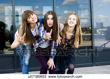 Stock Image - Three young women leaning forward in a row and making I love you hand gesture. Fotosearch