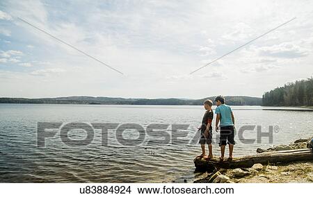 Two boys standing on fallen tree looking down into lake View Large Photo Image Picture - Two boys standing on fallen tree looking down into lake. Fotosearch