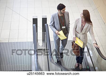 Stock Image - Two business colleagues on escalator a at conference centre. Fotosearch