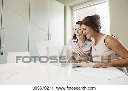 Two businesswoman laughing and looking at laptop View Large Photo Image Stock Image - Two businesswoman laughing and looking at laptop. Fotosearch