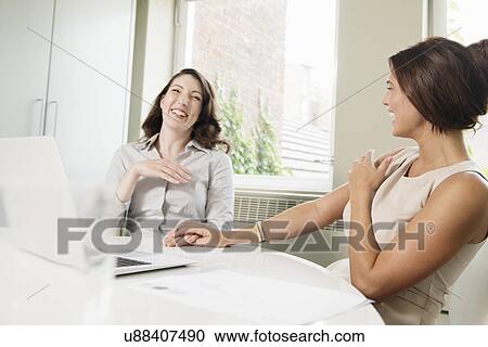 Stock Image - Two businesswoman laughing in office. Fotosearch