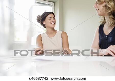 Stock Image - Two businesswomen chatting in conference room. Fotosearch