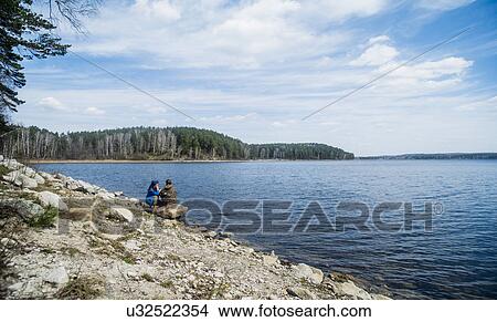 Two female hiking friends taking a break on lakeside View Large Photo Image Picture - Two female hiking friends taking a break on lakeside. Fotosearch
