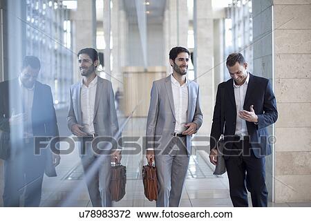 Stock Image - Two young businessmen walking and chatting in conference centre. Fotosearch