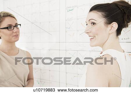 Stock Image - Two young businesswomen planning in office. Fotosearch