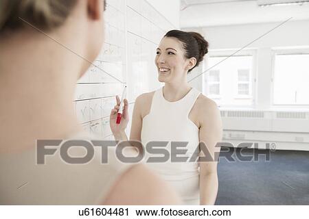 Two young businesswomen planning on whiteboard in office View Large Photo Image Stock Image - Two young businesswomen planning on whiteboard in office. Fotosearch