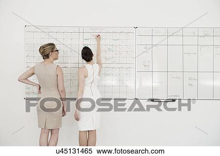 Stock Photography - Two young businesswomen planning on office whiteboard. Fotosearch