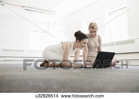 Two young businesswomen using laptop on floor in new office View Large Photo Image Picture - Two young businesswomen using laptop on floor in new office. Fotosearch