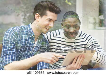Two young male friends looking at digital tablet behind window View Large Photo Image Stock Photography - Two young male friends looking at digital tablet behind window. Fotosearch