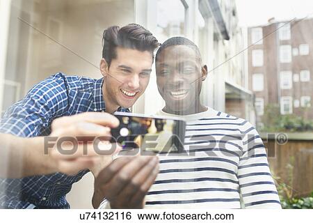 Stock Photograph - Two young male friends taking selfie behind patio glass. Fotosearch
