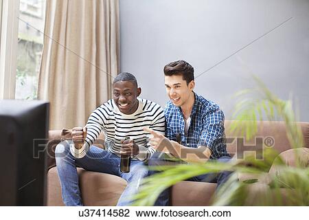 Two young men drinking beer and watching TV in living room View Large Photo Image Stock Image - Two young men drinking beer and watching TV in living room. Fotosearch