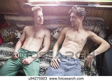 Stock Image - Two young men lying bare chested on bed. Fotosearch
