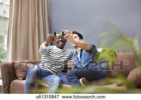 Two young men waking selfie with smartphone on living room sofa View Large Photo Image Stock Photo - Two young men waking selfie with smartphone on living room sofa. Fotosearch