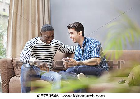 Two young men with smartphone on living room sofa View Large Photo Image Stock Photograph - Two young men with smartphone on living room sofa. Fotosearch
