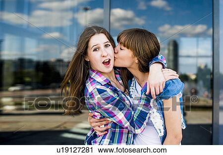 Stock Image - Two young women fooling around hugging with kiss on cheek. Fotosearch