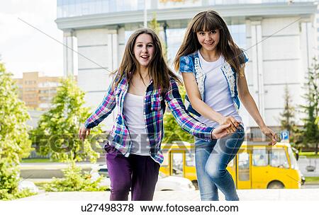 Stock Photo - Two young women holding hands and running in city. Fotosearch