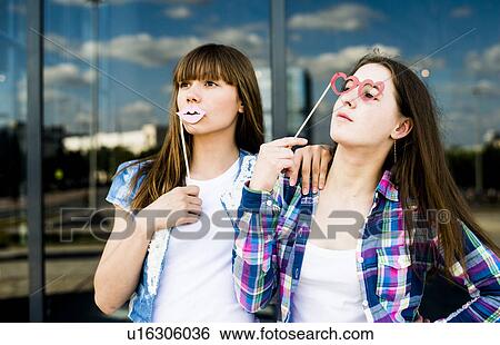 Stock Photograph - Two young women looking up with lip and spectacles costume masks. Fotosearch