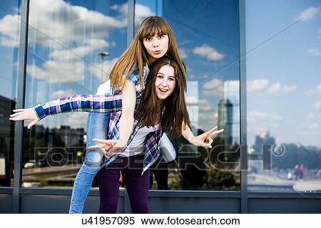 Two young women piggybacking and making peace signs View Large Photo Image Stock Photography - Two young women piggybacking and making peace signs. Fotosearch