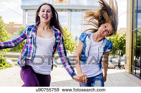 Stock Photo - Two young women shaking their hair and running in city. Fotosearch