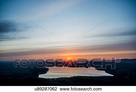 Stock Image - View of silhouetted sunset over distant lake. Fotosearch