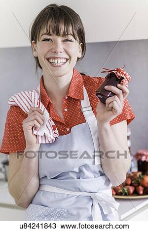 Stock Image - Woman holding up jar of homemade strawberry jam. Fotosearch