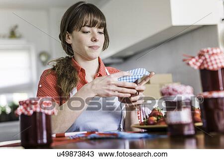 Stock Image - Woman packing homemade strawberry jam. Fotosearch