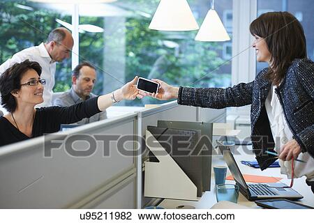 Stock Image - Woman passing smartphone to colleague. Fotosearch