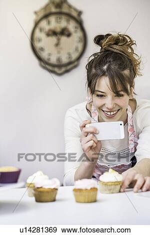 Stock Photo - Woman taking photograph of cupcakes with smartphone. Fotosearch
