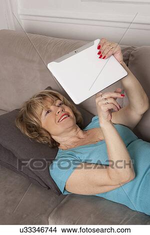 Picture - Woman using digital tablet on sofa. Fotosearch