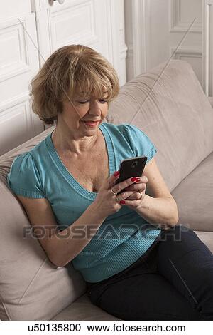 Stock Image - Woman using smartphone on sofa. Fotosearch
