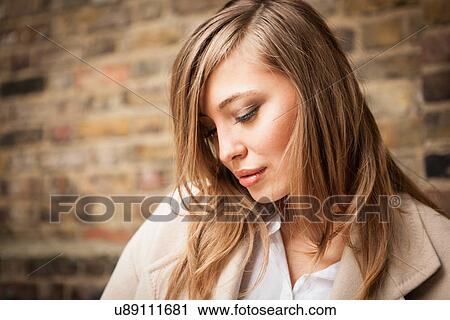 Stock Image - Woman with downcast eyes, brick wall in background. Fotosearch