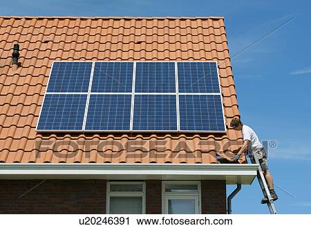 Stock Image - Worker checking installation of solar panels on roof of new home, Netherlands. Fotosearch