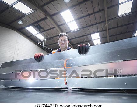 Stock Image - Worker inspecting newly cut parts in sheet metal factory. Fotosearch