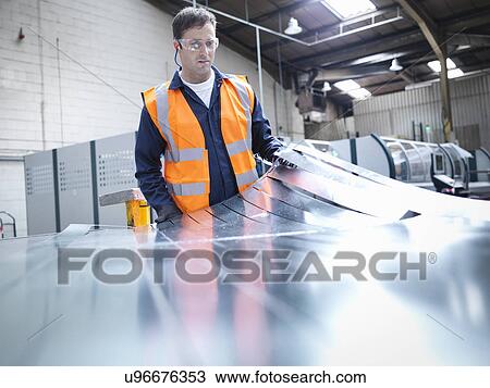 Stock Image - Worker inspecting newly cut parts in sheet metal factory. Fotosearch