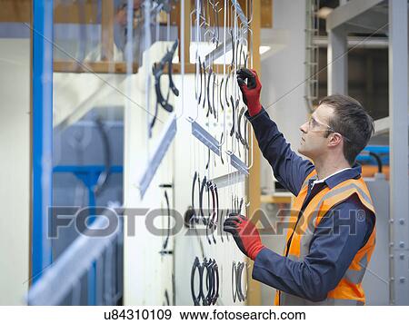 Stock Photo - Worker inspecting painted parts in sheet metal factory. Fotosearch