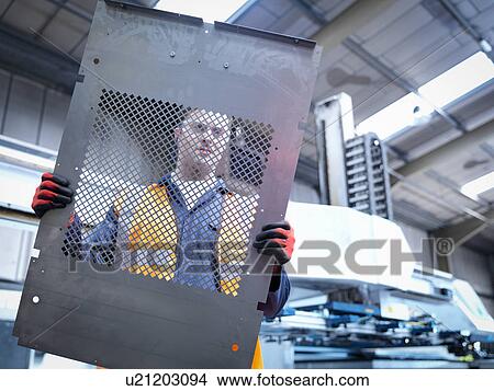 Picture - Worker inspecting parts next to robotic metal cutting machine in sheet metal factory. Fotosearch