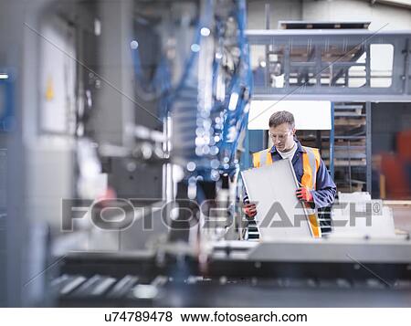 Stock Photo - Worker inspecting parts next to robotic metal cutting machine in sheet metal factory. Fotosearch