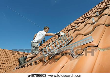 Stock Image - Worker installing framework for solar roof panels on new home, Netherlands. Fotosearch