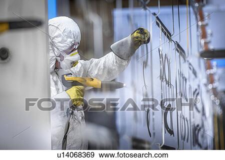 Stock Photo - Worker powder coating parts in paint spray booth in sheet metal factory. Fotosearch