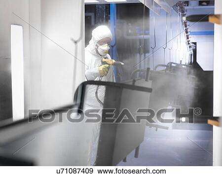 Stock Photo - Worker powder coating parts in paint spray booth in sheet metal factory. Fotosearch