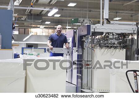 Stock Image - Worker using machine in paper packaging factory. Fotosearch