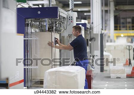Stock Image - Worker using machine in paper packaging factory. Fotosearch