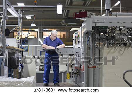 Stock Photo - Worker using machine in paper packaging factory. Fotosearch