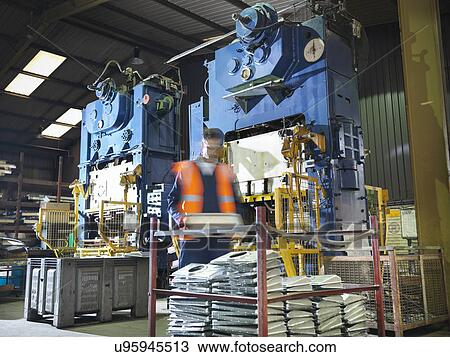 Stock Image - Worker with metal press in sheet metal factory. Fotosearch